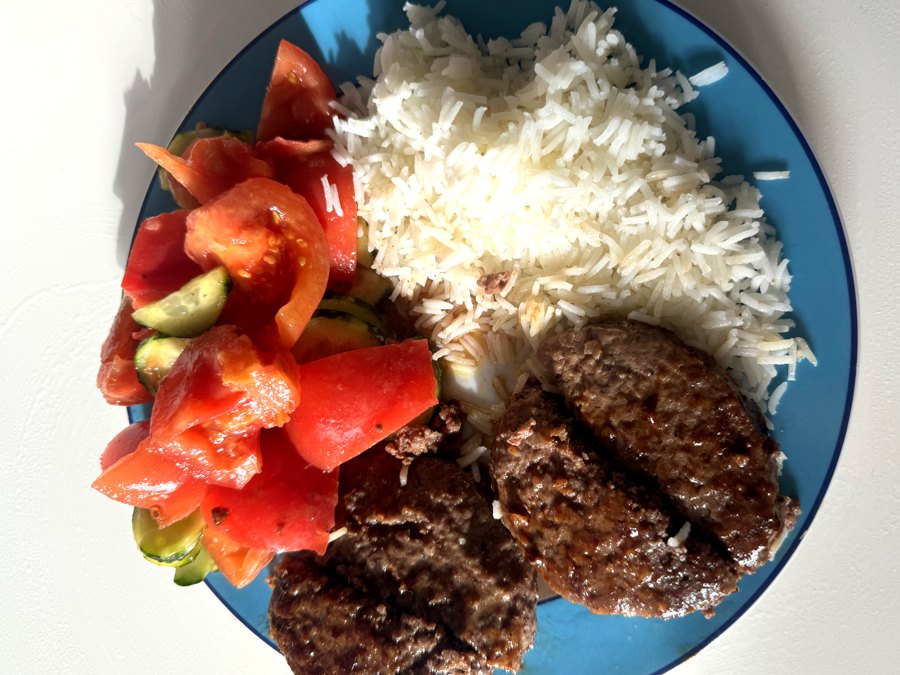 Lunch from the plan: beef patties, white rice and tomato salad on a blue plate.